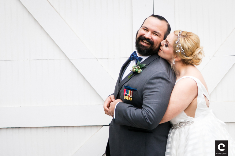 A beautiful blonde bride hugs her groom and kisses him on the cheek during their Allan House Winter Wedding photography session