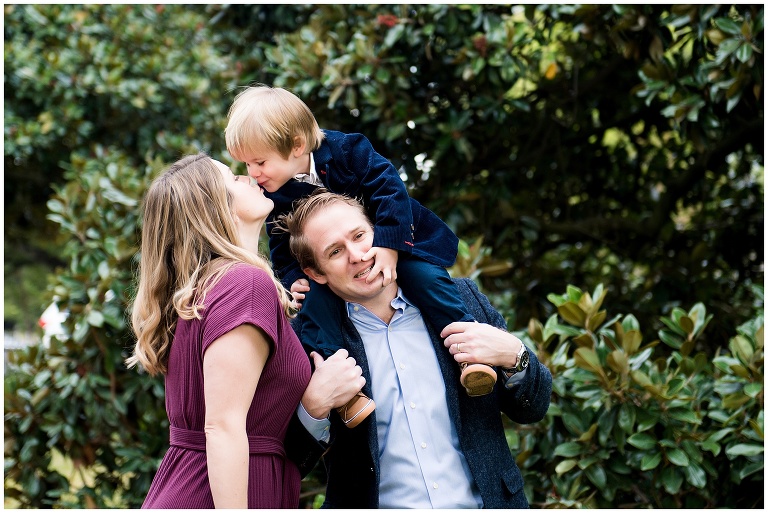 toddler son kissing his mom on dad's shoulders